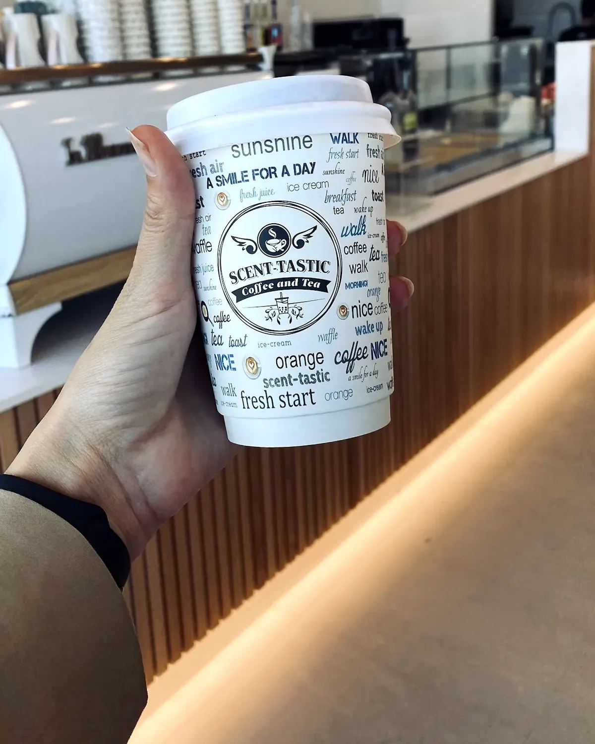 A hot coffee in their A Smile For A Day cup, held up at the counter by the white La Marzocco